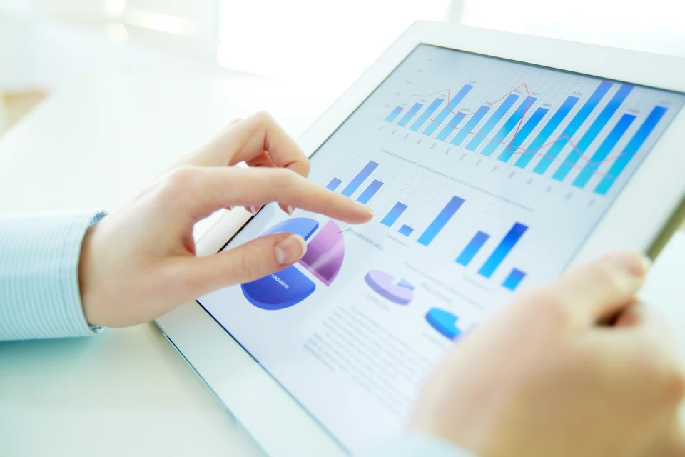 Scène de bureau avec mains utilisant une tablette tactile affichant des graphiques et données analytiques